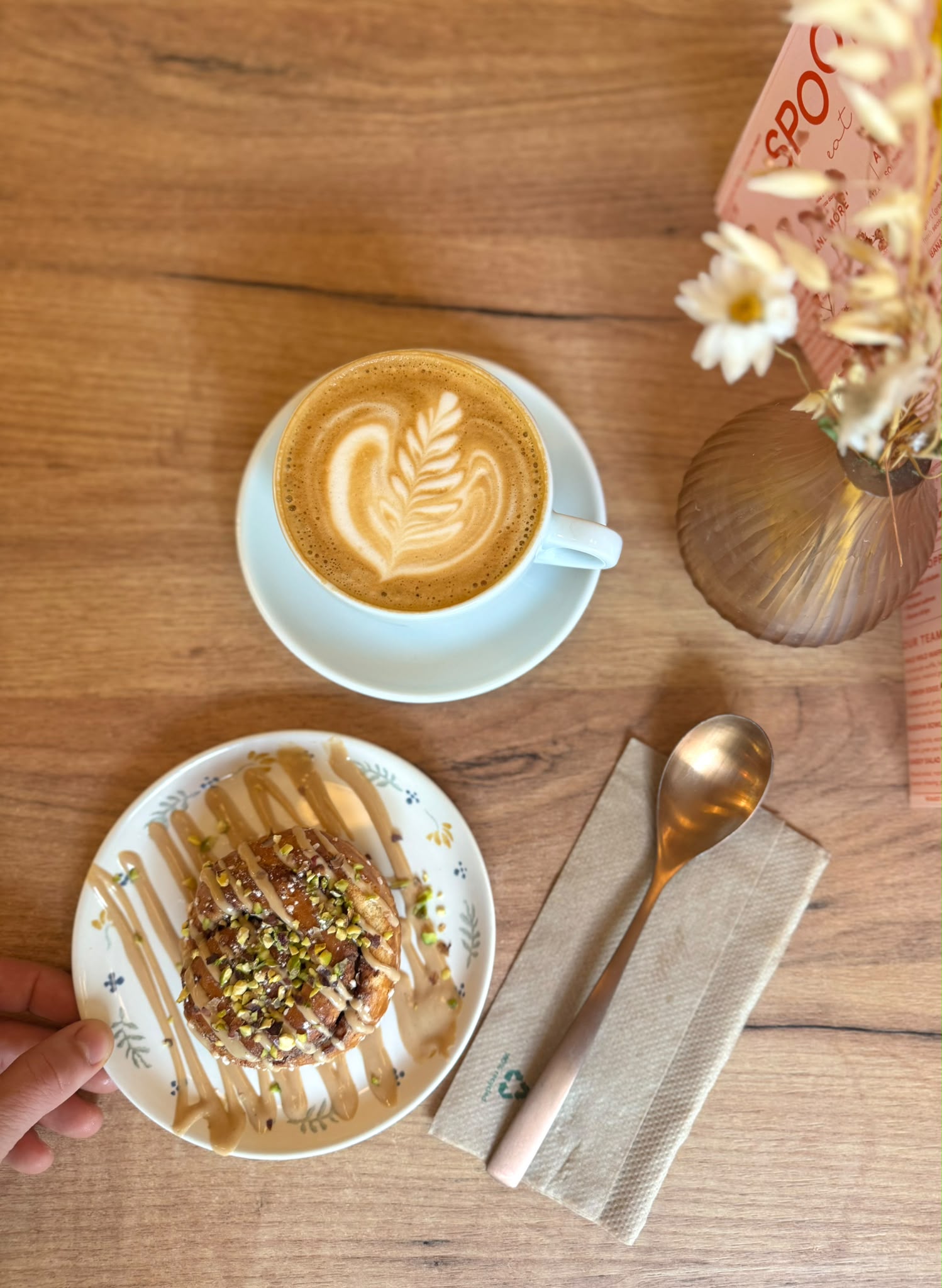 Specialty coffee met latte art en een huisgemaakt wafeltje op een houten tafel bij Spoons