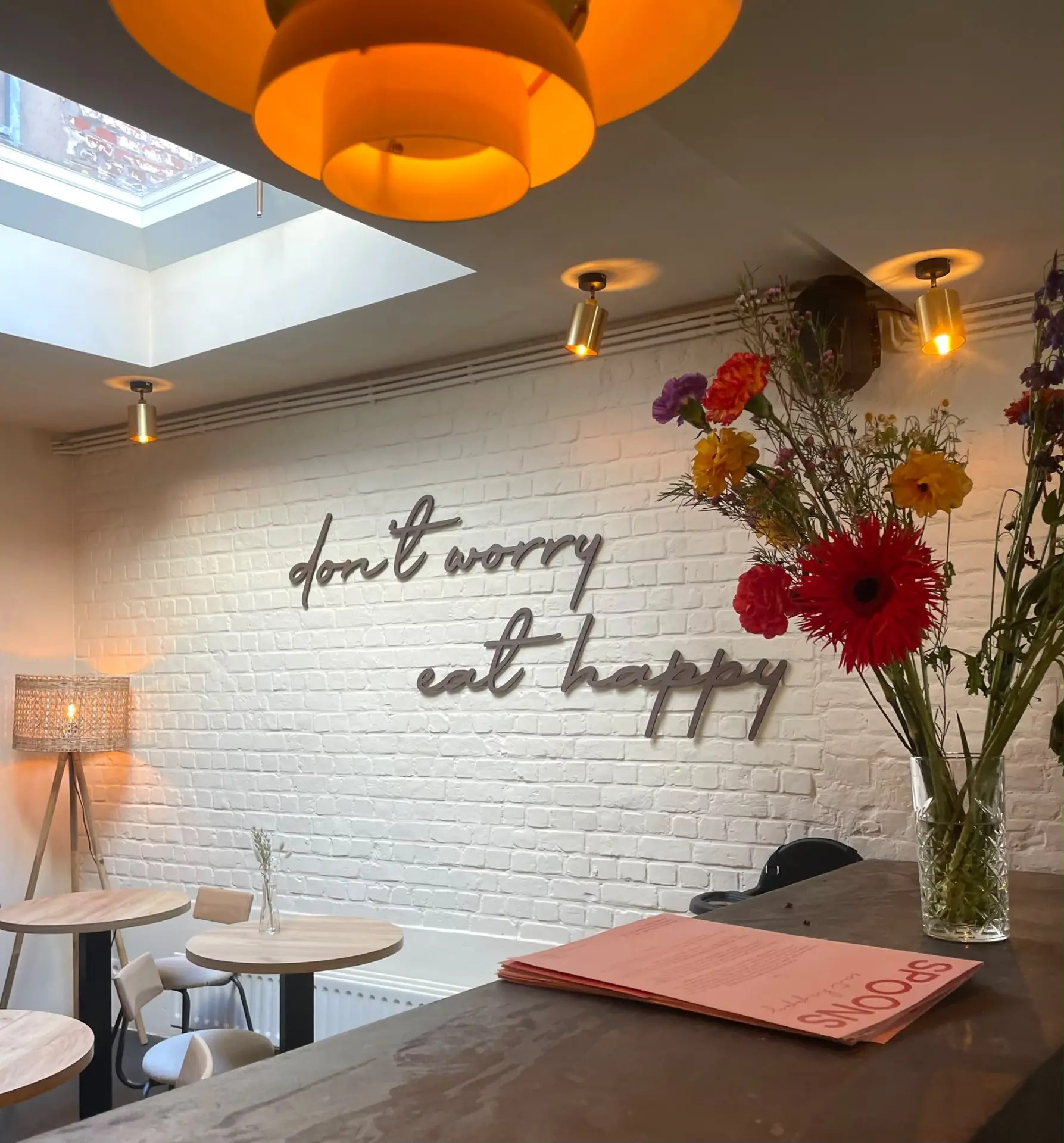 De muur met don’t worry, eat happy bij Spoons, met kleurige bloemen en oranje lampen
