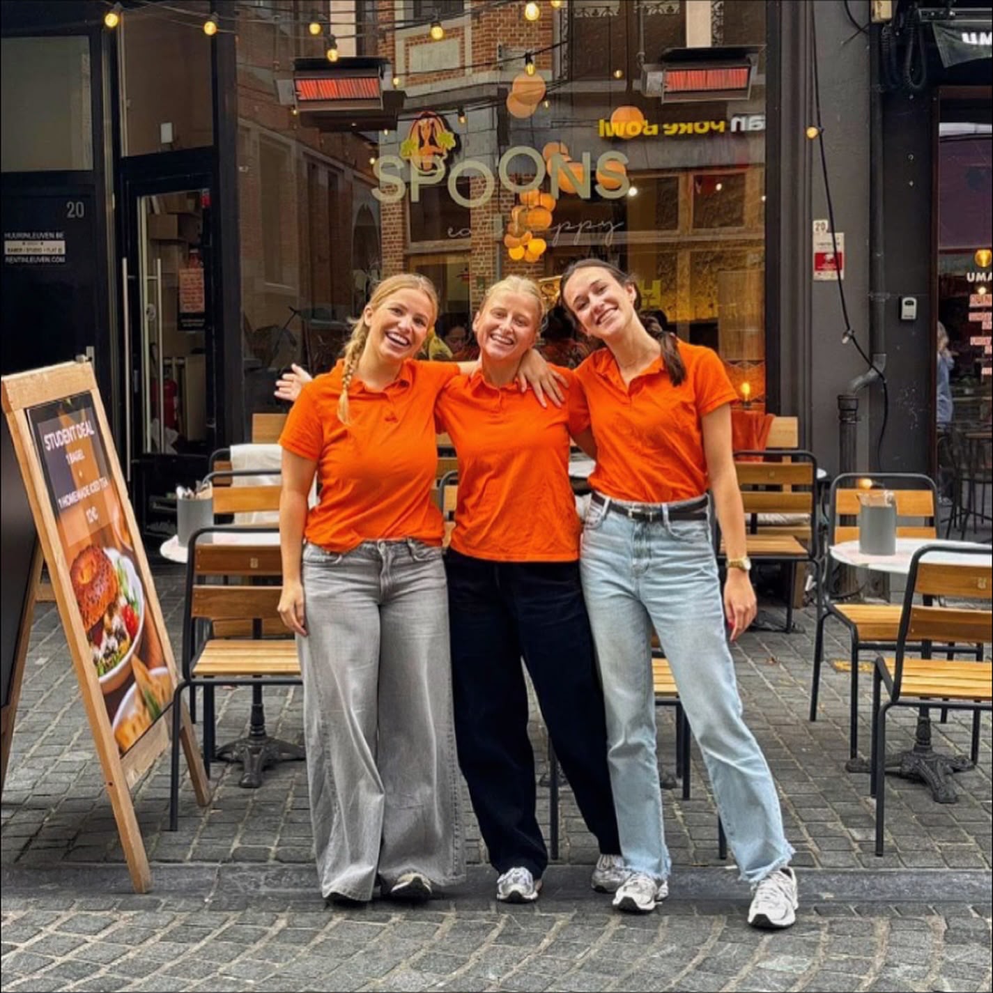 Drie Spooners in oranje polo's voor de gevel van Spoons in de Tiensestraat