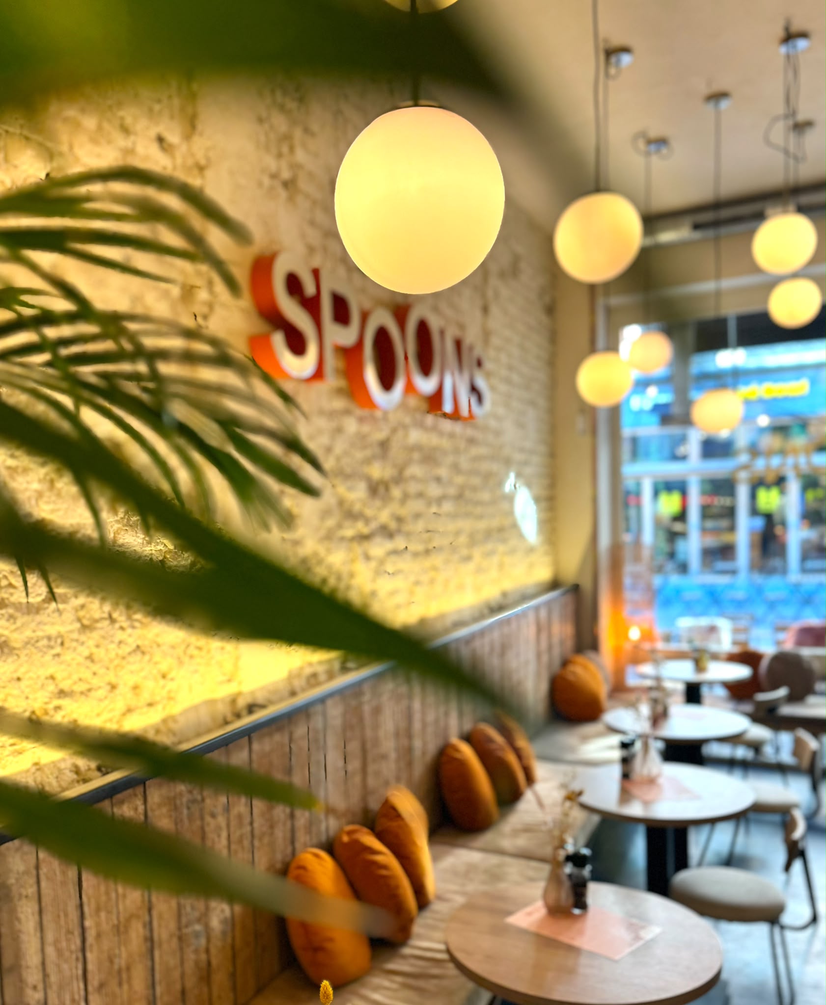 Licht interieur van Spoons met planten, houten tafels en rode SPOONS letters